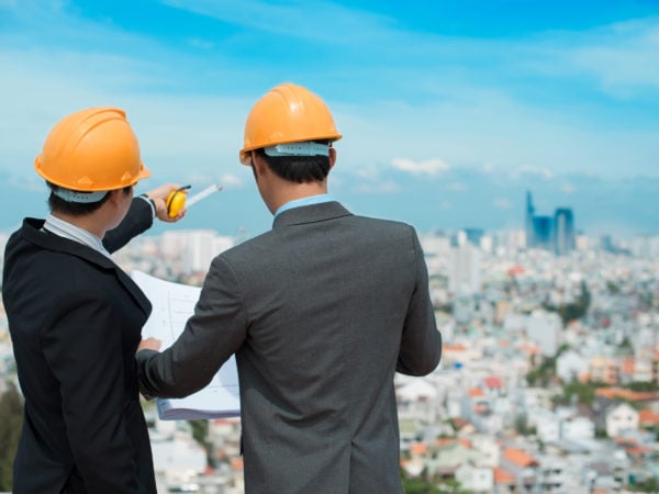 Businessmen in hardhats taking a look at the blueprint in urban environment